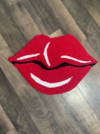 a red and white crocheted lips rug on a wooden floor